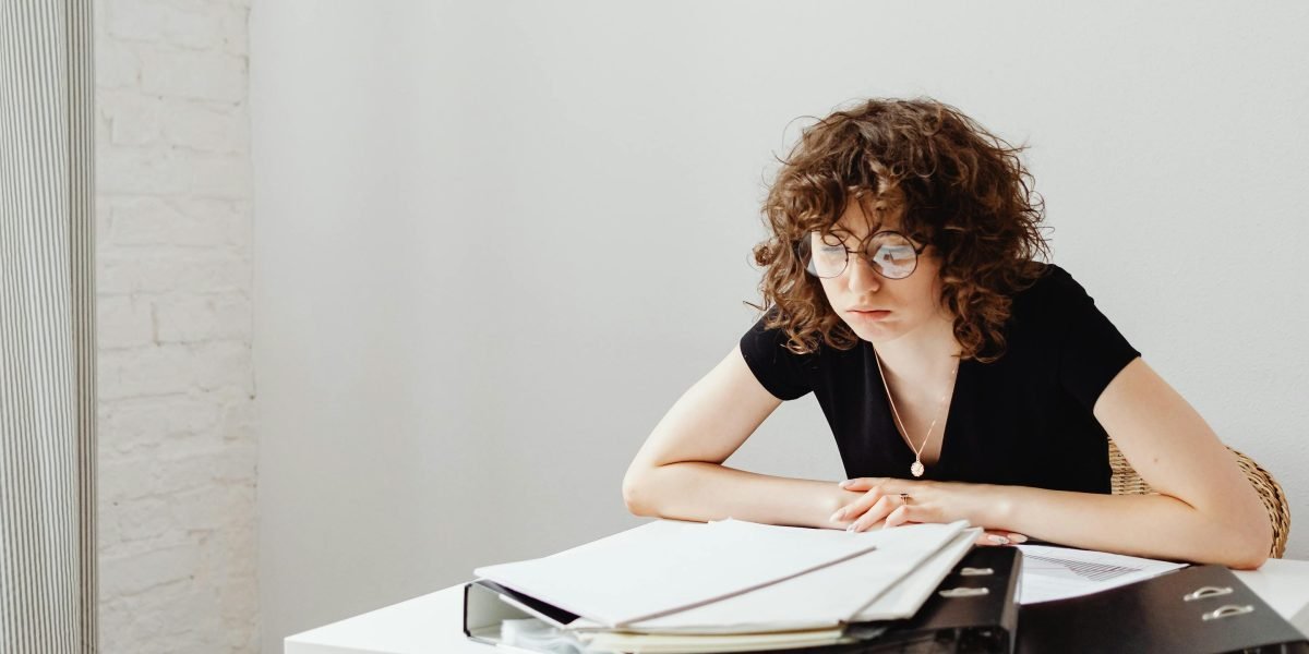 A healthcare professional looking thoughtful, surrounded by paperwork, symbolizing the administrative burden in family medicine.